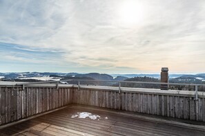 Una terraza de madera con barandilla, con vistas a un paisaje montañoso y cielo despejado.
