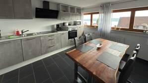 Een moderne keuken met grijze kastjes, een houten eettafel en uitzicht op zee door een raam.