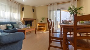 A living room with a sofa, a dining table with chairs, a fireplace, and a view through a large window. - Vacation home Golfa by Interhome (Deltebre)