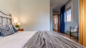 A bedroom with a bed, a bedside table with a lamp, a window with curtains, and a view of a hallway. - Vacation home Golfa by Interhome (Deltebre)
