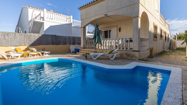 A swimming pool with lounge chairs, a covered patio, and a building with a tiled roof. - Vacation home Golfa by Interhome (Deltebre)