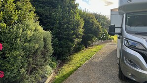 A truck parked beside a gravel path with dense foliage and a clear sky.
