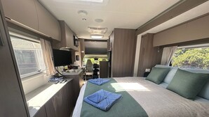 A compact RV interior with a kitchenette, a bed with green bedding, and a window providing natural light.