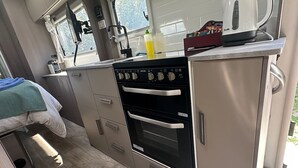 A compact kitchenette with a stove, oven, and a Breville kettle.
