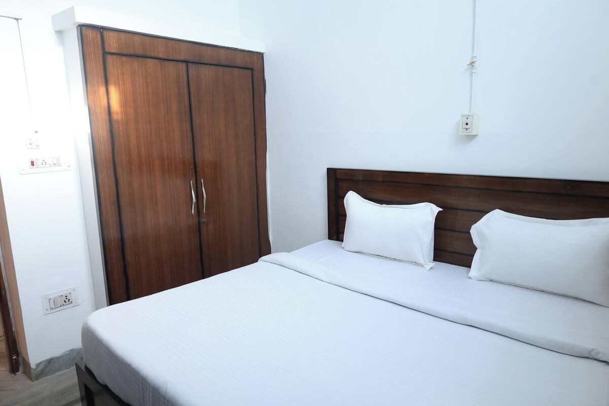 Habitació d'hotel amb un armari de fusta, un llit amb roba de llit blanca i una presa elèctrica.