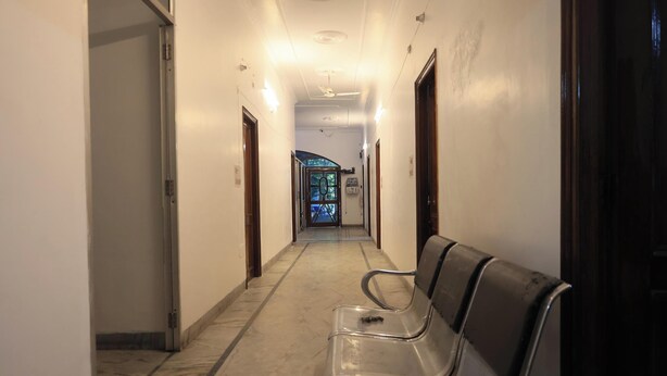 Un pasillo de hotel con un banco, puertas y vista a otra habitación.