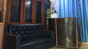 Una habitación con un sofá de cuero negro, un armario de madera, un ventilador de techo y un reloj en la pared.