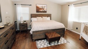 Une chambre à coucher avec un lit en bois, une table de chevet, une lampe et une fenêtre avec des rideaux.
