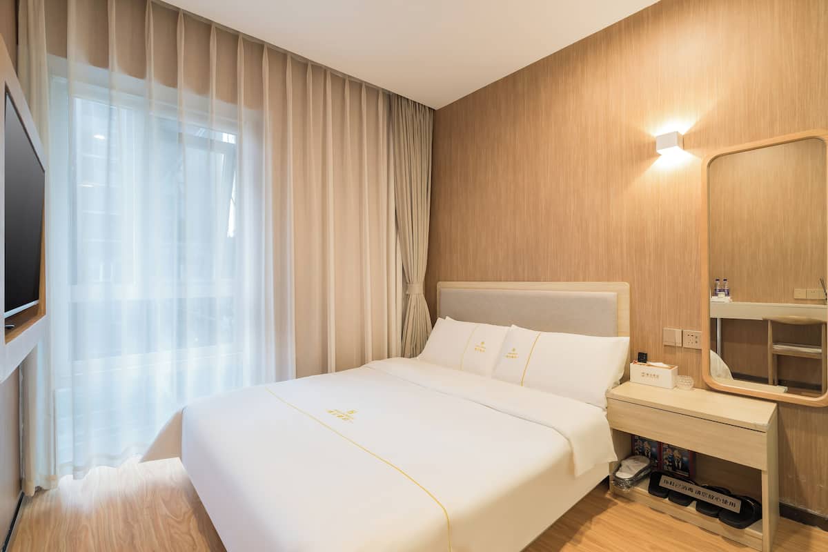 A hotel room with a large bed, a bedside table with a mirror, a TV, and a shoe rack.