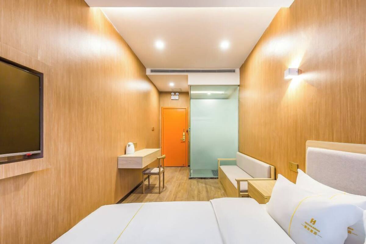 A hotel room with a bed, a TV, a small table with a chair, a sink, and a door leading to a bathroom.