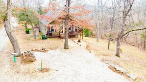 Une cabane dotée d’une terrasse, entourée d’arbres et bordée d’une allée en gravier.