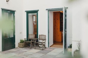 Un petit espace extérieur avec une table et des chaises en bois, une porte verte et une porte en bois donnant sur l’intérieur.