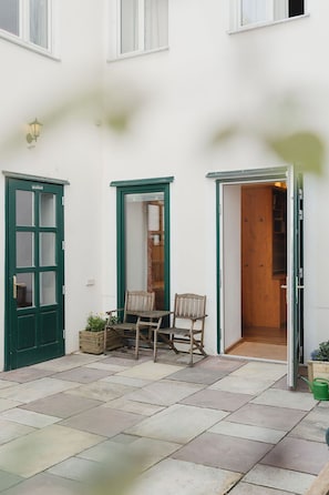 Um pátio com uma mesa e cadeiras de madeira, uma porta verde e uma porta de madeira que dá para o interior.