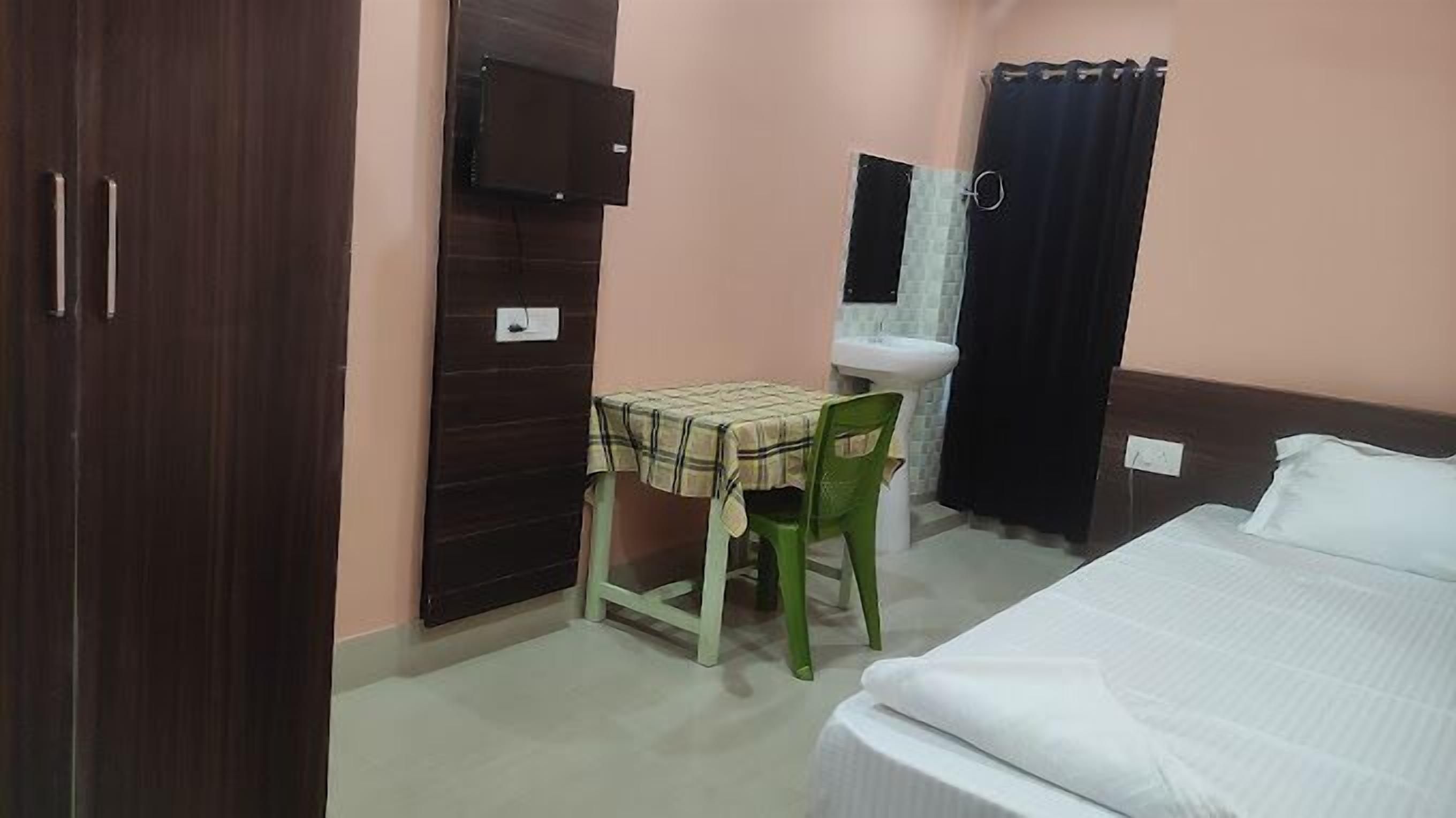 Une chambre à coucher avec un lit, une table et une chaise, un téléviseur fixé au mur, et une salle de bain avec un lavabo et un rideau de douche.