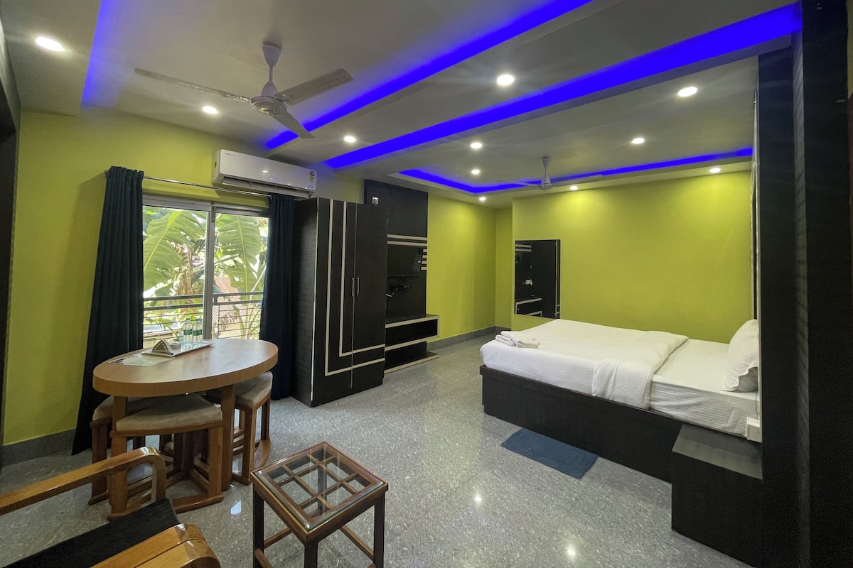 Quarto de hotel com cama, escrivaninha, cadeira, televisão e janela com cortinas.
