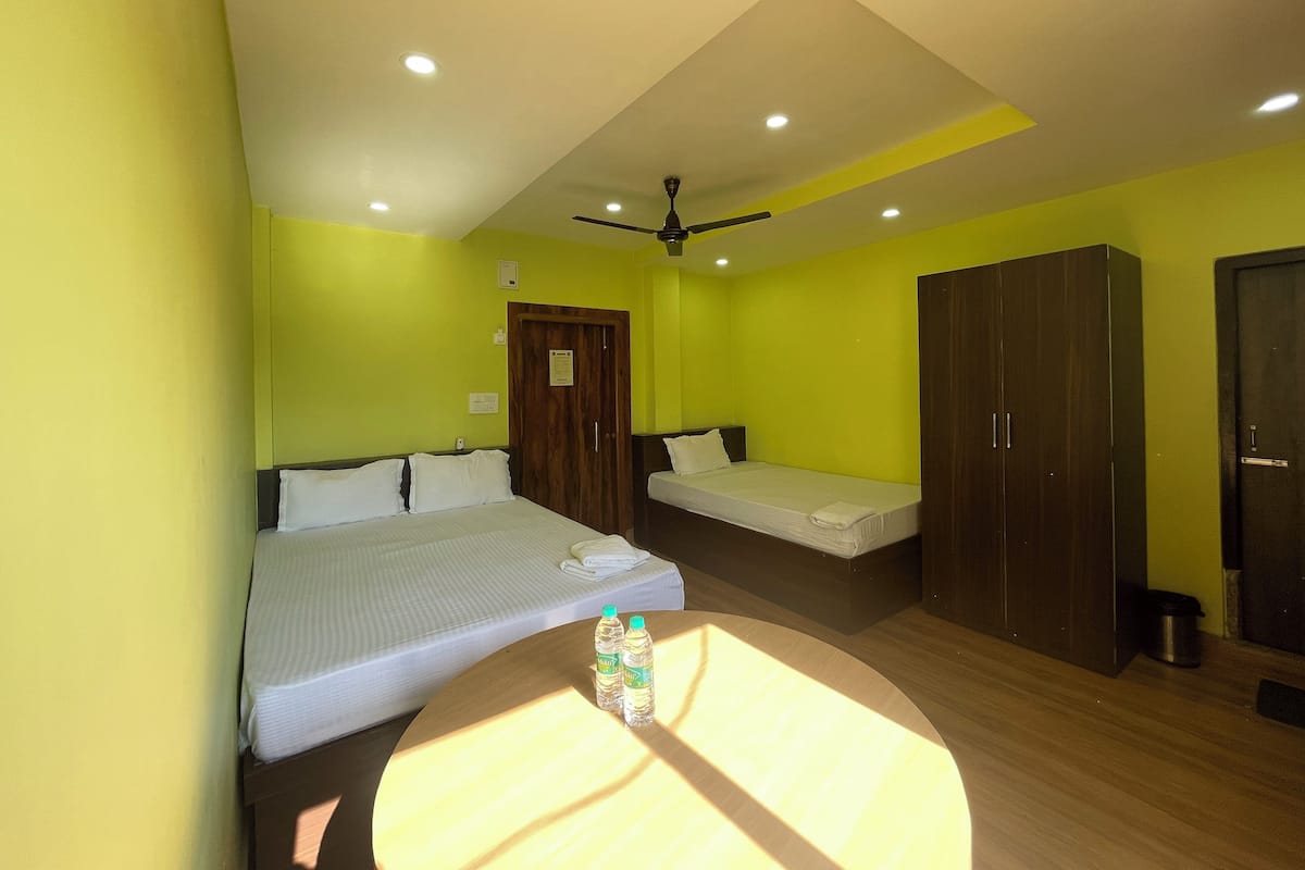 Quarto de hotel com duas camas de solteiro, um guarda-roupa de madeira, um ventilador de teto e uma mesa redonda com garrafas de água.