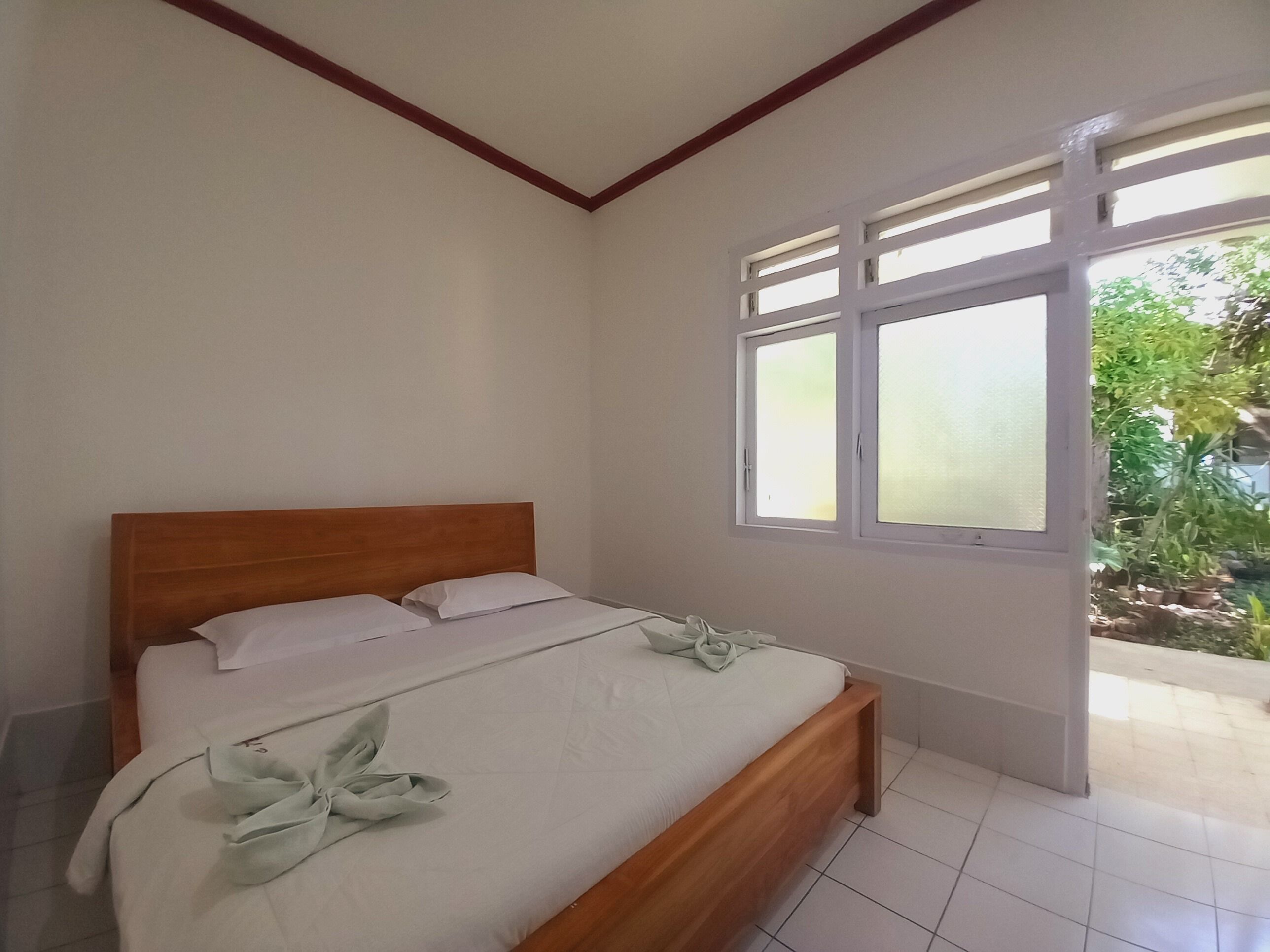 A bedroom with a wooden bed, white linens, and a window with frosted glass.
