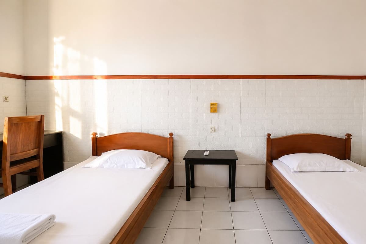 A room with two single beds, a small table, a chair, and a white brick wall.