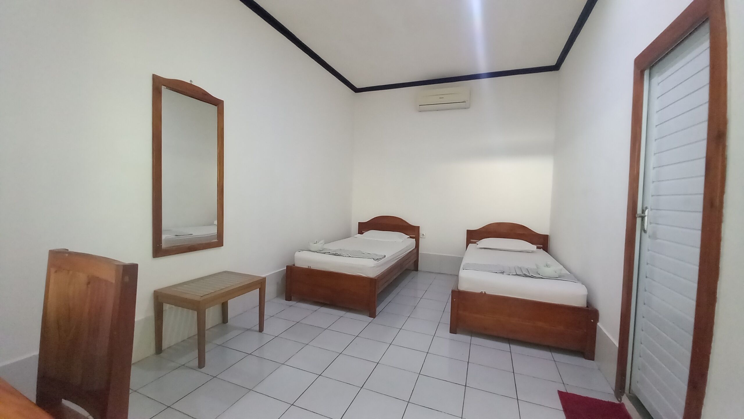 A small, clean room with two wooden beds, a wooden bench, a mirror, and a door.