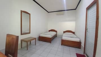 A small, clean room with two wooden beds, a wooden bench, a mirror, and a door.