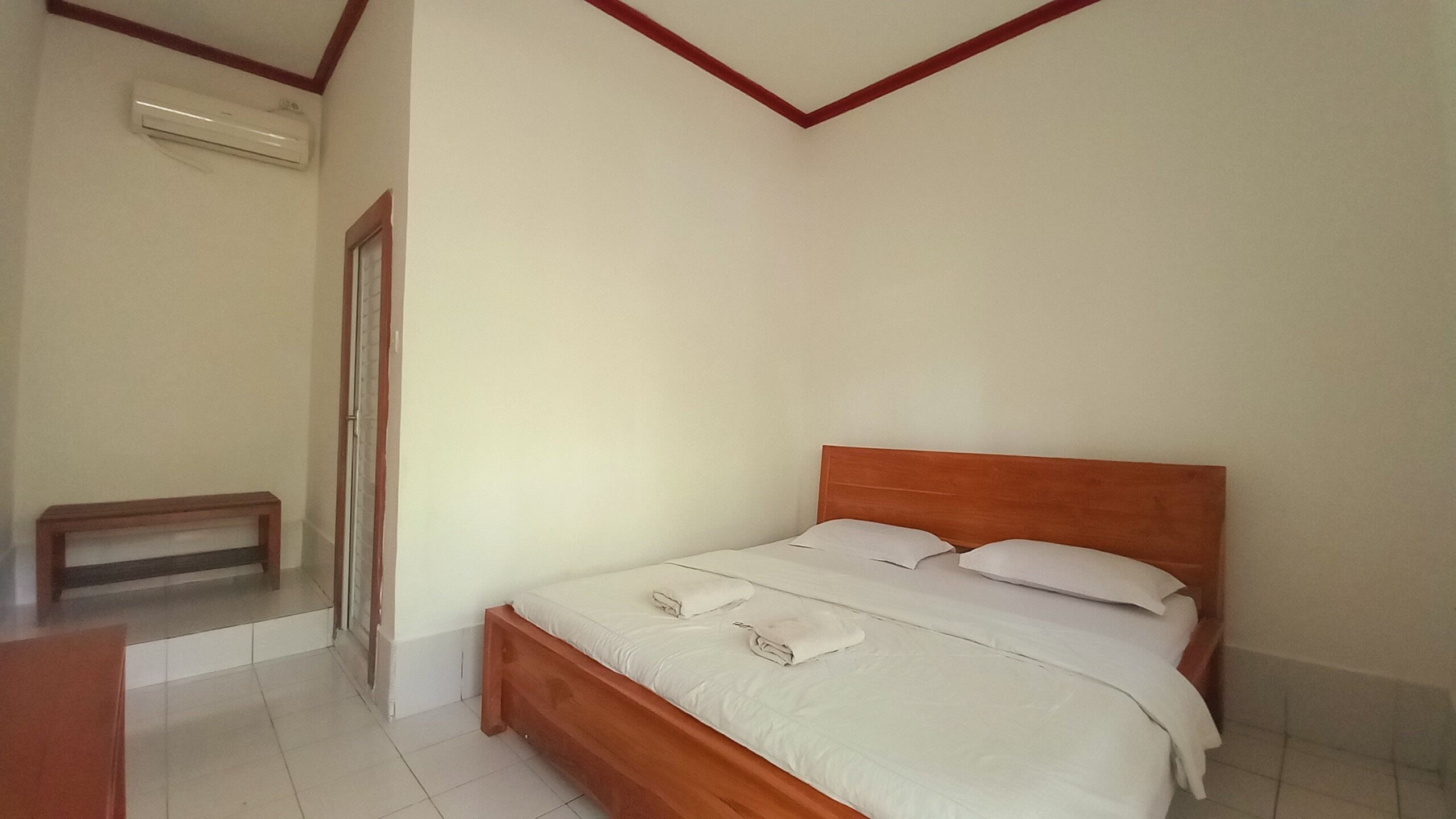 A bedroom with a wooden bed, white linens, a small bedside table, and a wall-mounted air conditioner.