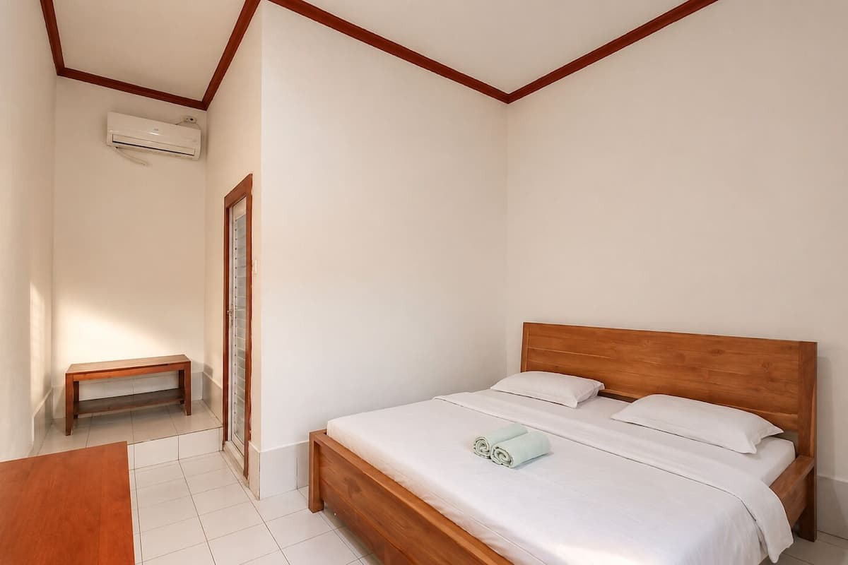 A bedroom with a wooden bed, a small bench, and a window.