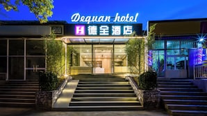 Exterior del Hotel Dequan, con una entrada bien iluminada, una escalera que conduce a las puertas y una vista clara de la señalización del hotel.