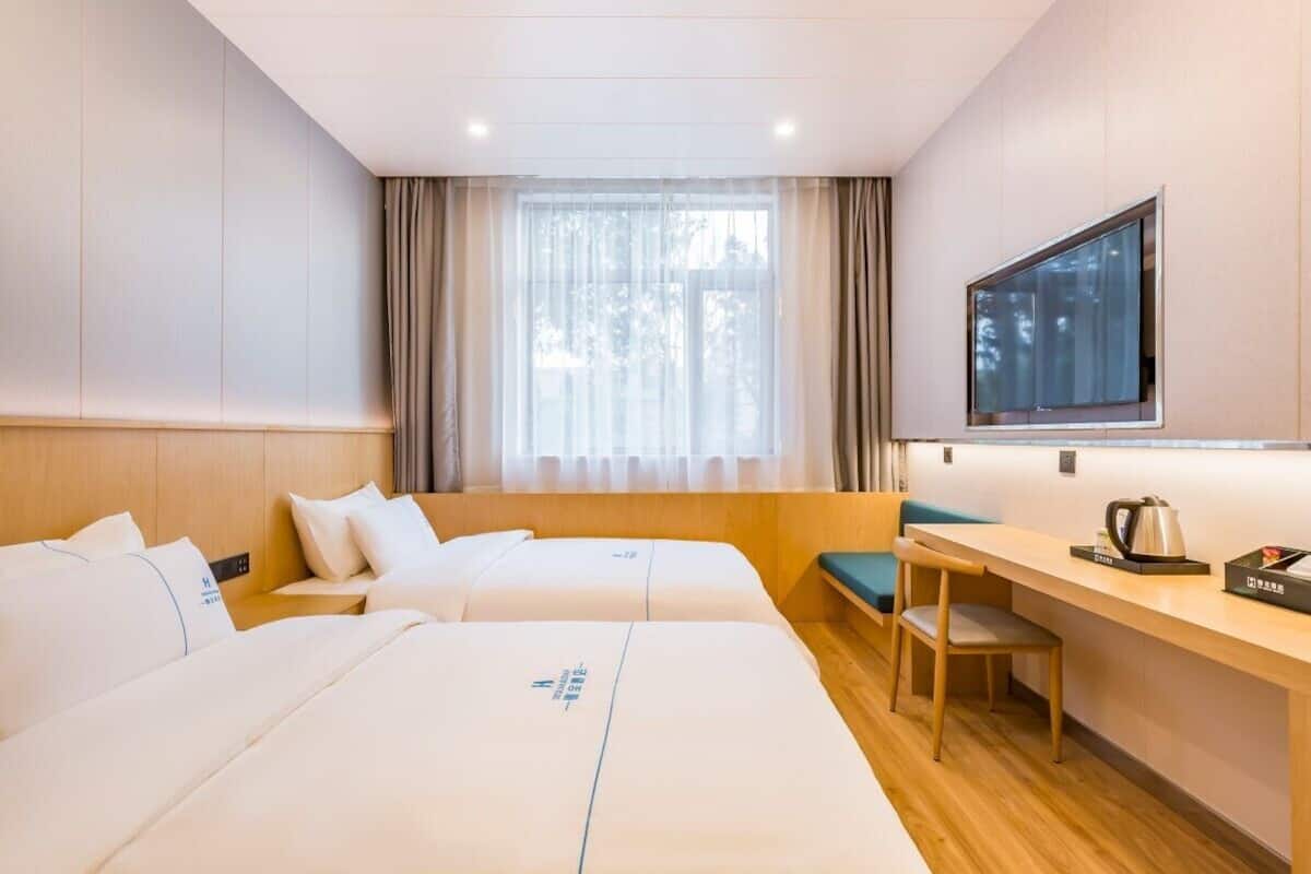 Habitación de hotel con dos camas, un escritorio, una silla, un televisor y una ventana con cortinas.