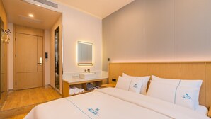 Habitación de hotel con cama, mesita de noche, espejo, armario de madera y baño con lavabo y espacio para toallas.