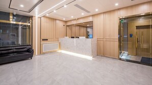 Un área de recepción moderna con un mostrador de mármol, un sofá de cuero negro y un ascensor de vidrio.