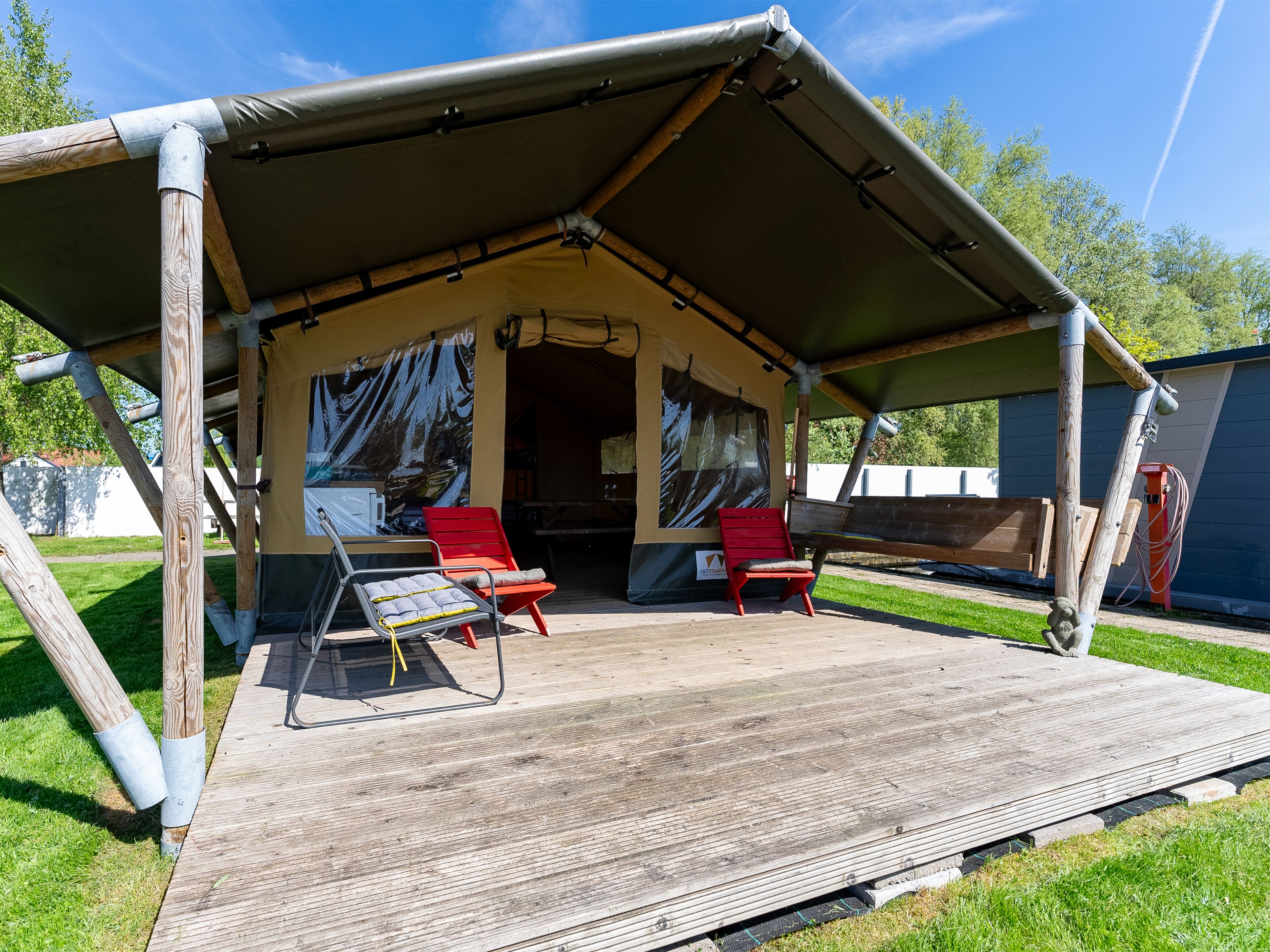 A tented outdoor area with a wooden deck, two red chairs, and a table.