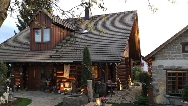 A rustic log cabin with a stone extension, a covered outdoor seating area, and a fire pit.