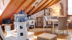 A model lighthouse in a cozy, well-lit room with wooden beams, a dining area, and a view of the outdoors.