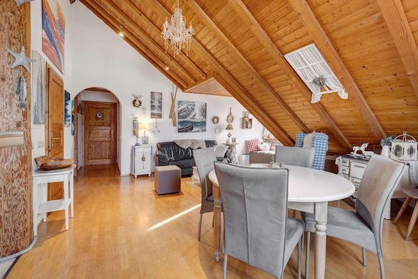Une pièce mansardée avec un plafond en bois, une table à manger avec des chaises, un canapé et divers éléments de décoration murale.