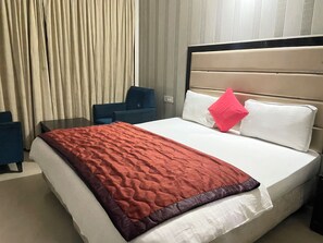A hotel room with a bed, a desk, a chair, and a window with curtains. - Hotel Ek Noor Residency (Mohali)