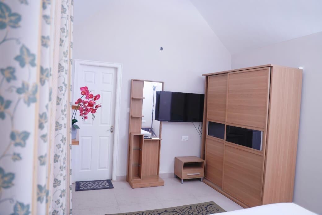A bedroom with a wooden wardrobe, a TV mounted on the wall, and a small bedside table.