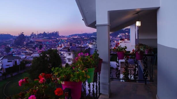 A balcony with potted plants and a view of a cityscape at dusk. - Aanvis Inn boutique home stay (Ootacamund)