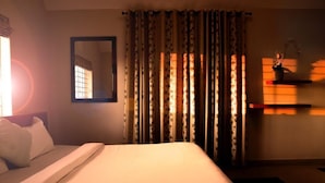 A bedroom with a bed, a mirror, curtains, and a shelf with a plant. - Aanvis Inn boutique home stay (Ootacamund)