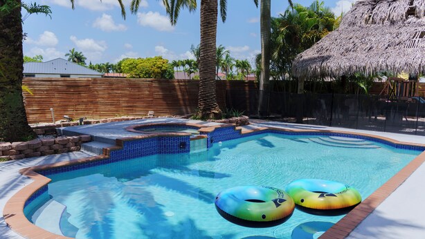 A swimming pool with a hot tub, surrounded by palm trees and a wooden fence. - Miami 5BR Pool Home ● BBQ ● Pool ● Coffee Bar ● Kid-Friendly ● Whirlpool Tub (Miami)