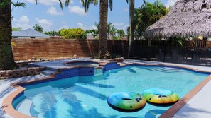 A swimming pool with a hot tub, surrounded by palm trees and a wooden fence.