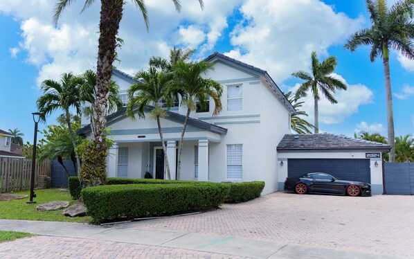 A two-story house with a garage, surrounded by palm trees and a well-maintained lawn.