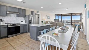A modern kitchen with grey cabinets, a central island, and a dining area with white chairs.