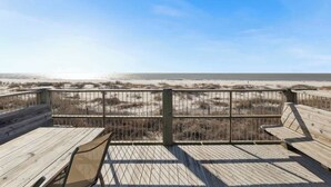 A wooden deck with benches overlooking a beach with dunes and the ocean.