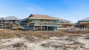 A beachfront house with multiple decks and a sandy beach in the foreground.