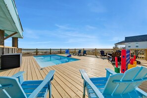 A wooden deck with a pool, lounge chairs, and a basketball hoop.