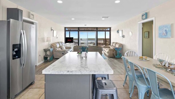 A modern kitchen with a central island, stainless steel refrigerator, and a dining area with blue chairs.