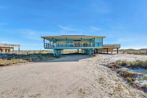 A beach house with a flat roof, multiple balconies, and a sandy surrounding.
