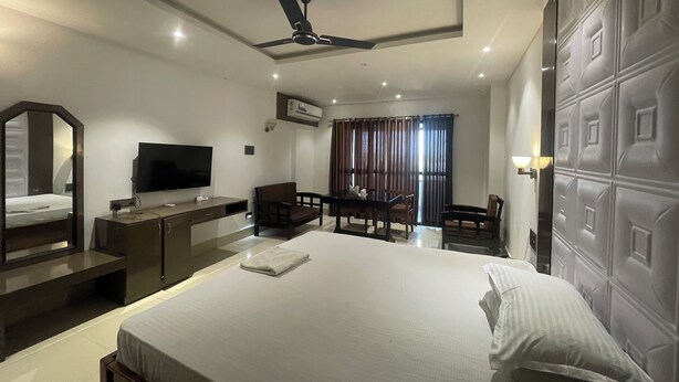 Ein Hotelzimmer mit Bett, Schreibtisch, Stuhl, Fernseher und Deckenventilator.
