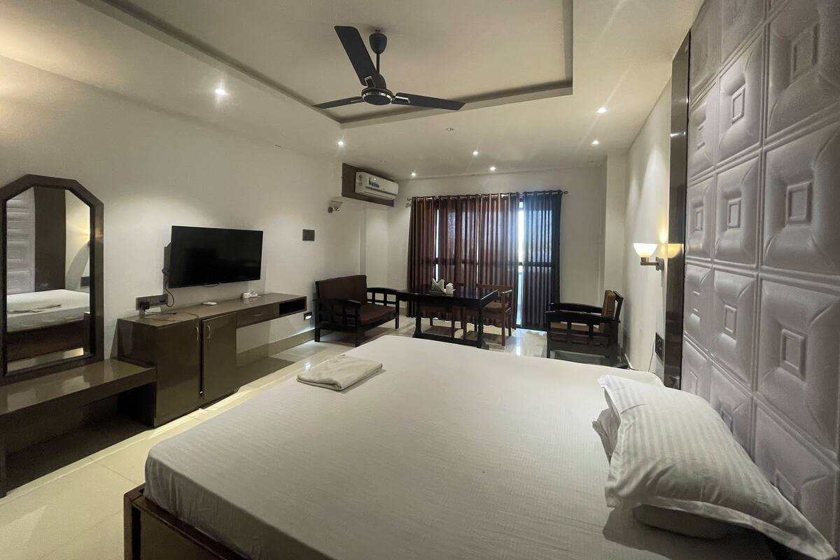 Une chambre d’hôtel équipée d’un lit, d’un bureau, d’une chaise, d’une télévision et d’un ventilateur de plafond.