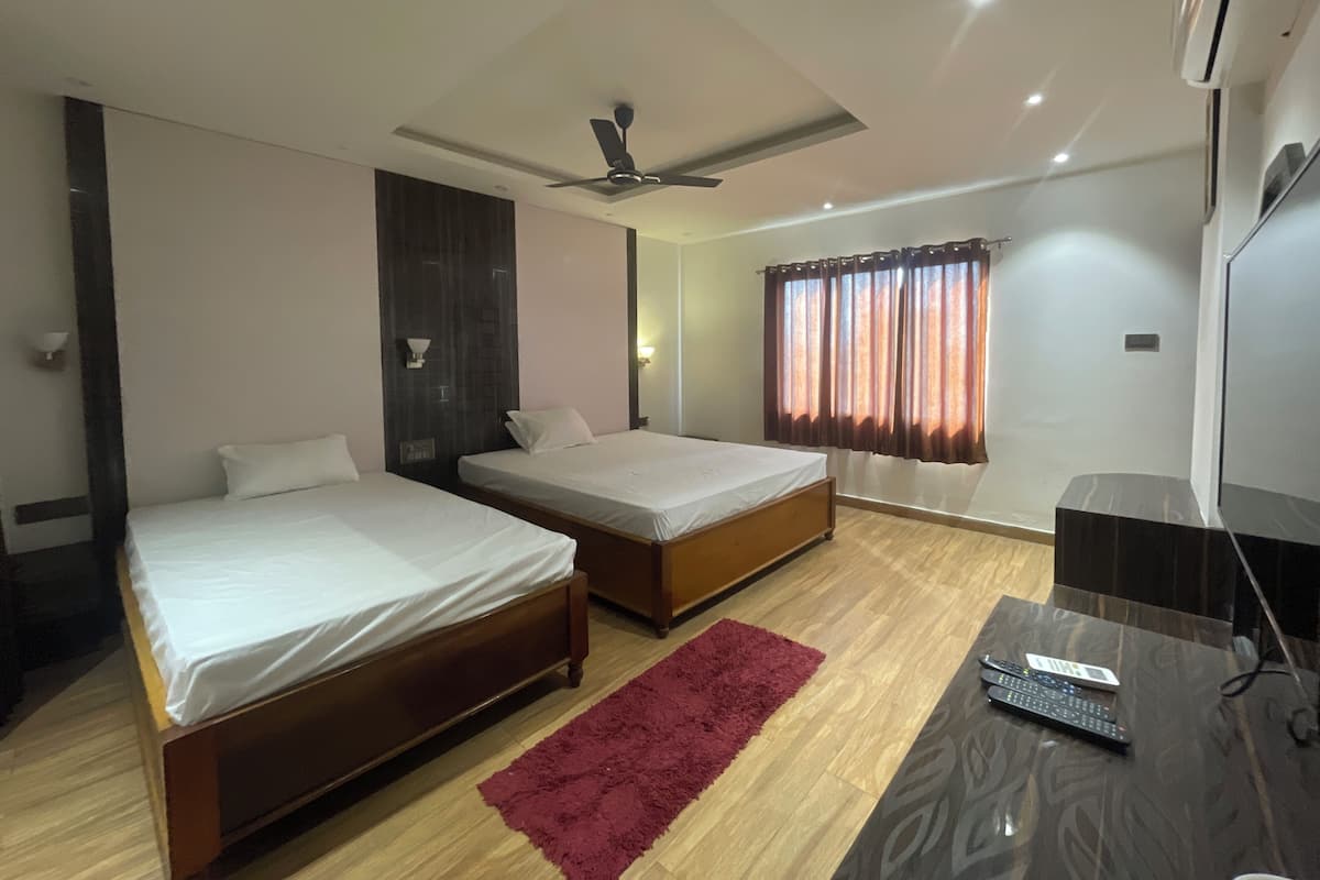 Une chambre d’hôtel avec deux lits simples, un bureau avec un ordinateur, un tapis rouge, un ventilateur de plafond et une fenêtre avec des rideaux.